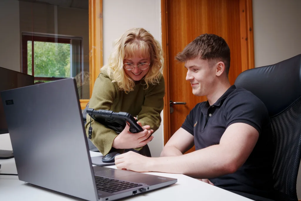 A man and a woman are at a desk, focused on reviewing content displayed on an iPad.