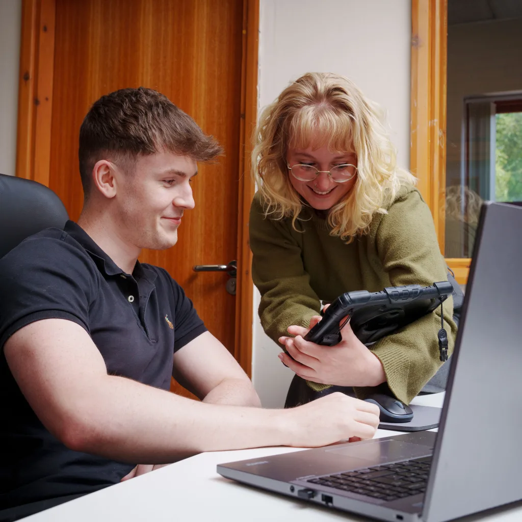 A man and a woman are at a desk, focused on reviewing content displayed on an iPad.