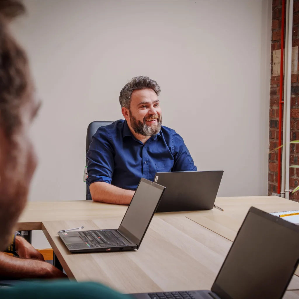 A man leading a meeting at a table, with two laptops for presentations and discussions.